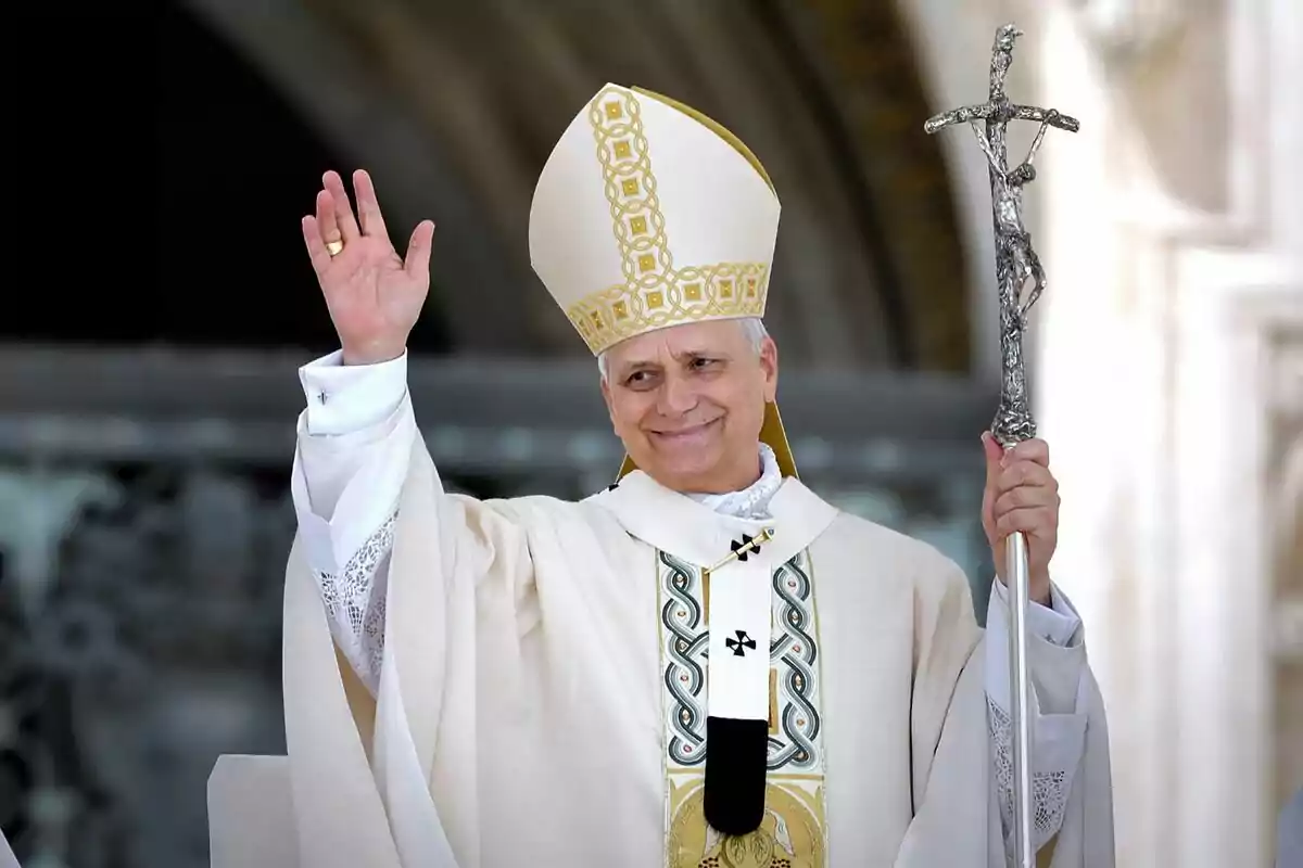 Obispo católico sonriente con mitra y báculo levantando la mano en señal de saludo Obispo católico sonriente con mitra y báculo levantando la mano en señal de saludo