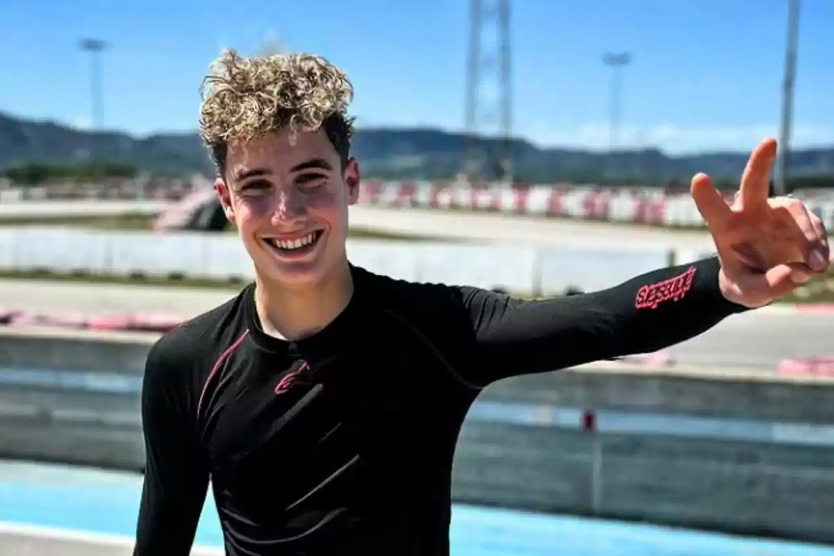 Jove somrient amb samarreta negra de màniga llarga aixecant la mà i fent el signe de la pau en una pista de curses a l’aire lliure Jove somrient amb samarreta negra de màniga llarga aixecant la mà i fent el signe de la pau en una pista de curses a l’aire lliure