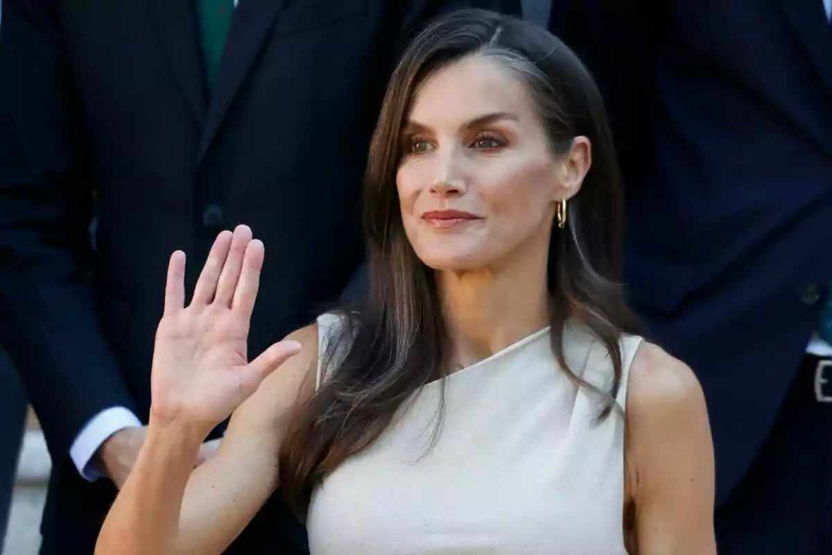 Mujer de cabello largo y oscuro con vestido claro saludando con la mano levantada Mujer de cabello largo y oscuro con vestido claro saludando con la mano levantada