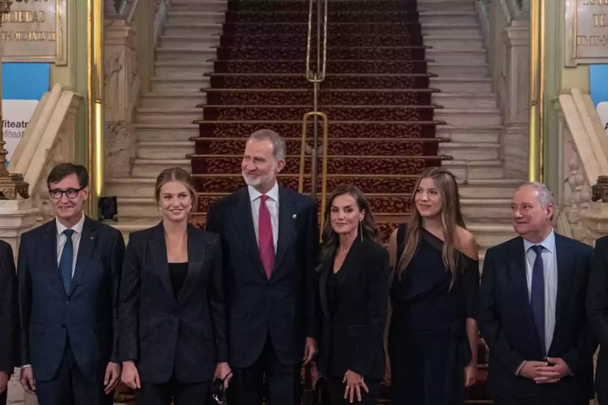 Grupo de personas elegantemente vestidas posando frente a una escalera alfombrada en un edificio histórico Grupo de personas elegantemente vestidas posando frente a una escalera alfombrada en un edificio histórico