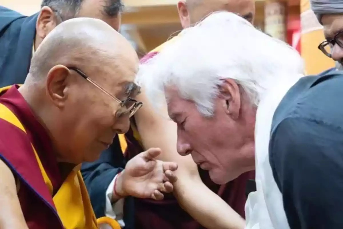 Richard Gere y el Dalái Lama se inclinan tocando sus frentes en un gesto de respeto y cercanía, rodeados de otras personas en un ambiente solemne. Richard Gere y el Dalái Lama se inclinan tocando sus frentes en un gesto de respeto y cercanía, rodeados de otras personas en un ambiente solemne.