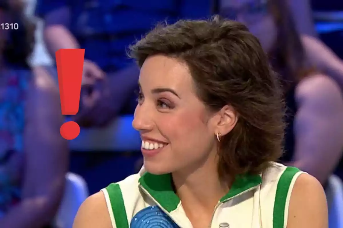 Rosa joven sonriendo en un programa de televisión con un gran signo de exclamación rojo a su lado