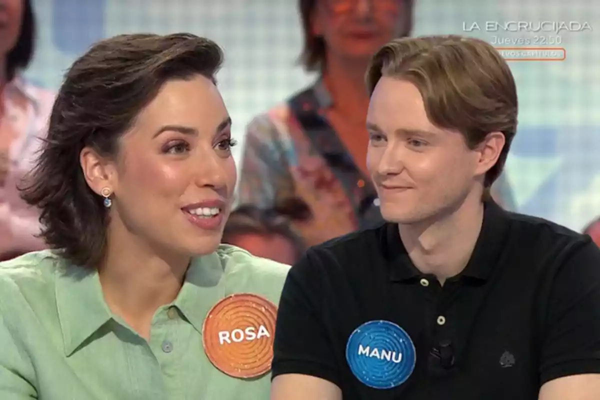 Dos concursants somriuen i conversen en un programa de televisió, cadascun porta una xapa amb el seu nom, Rosa i Manu, mentre el públic observa al fons.