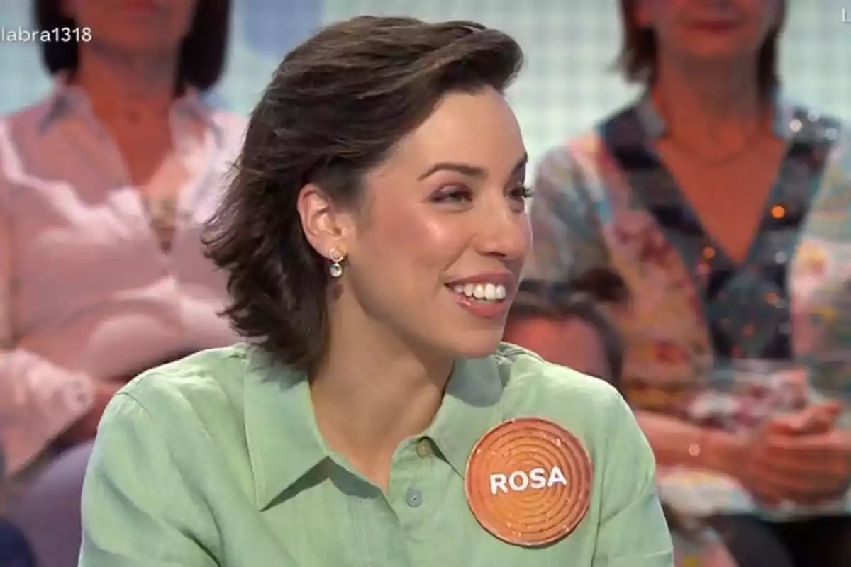 Dona somrient amb cabell curt i camisa verd clar participant en un programa de televisió amb una placa que diu Rosa Dona somrient amb cabell curt i camisa verd clar participant en un programa de televisió amb una placa que diu Rosa