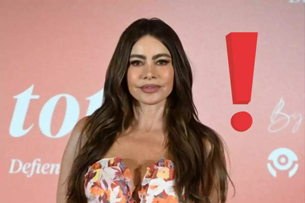 Long-haired woman with loose hair wearing a floral dress posing in front of a pink background with a large red exclamation mark next to her