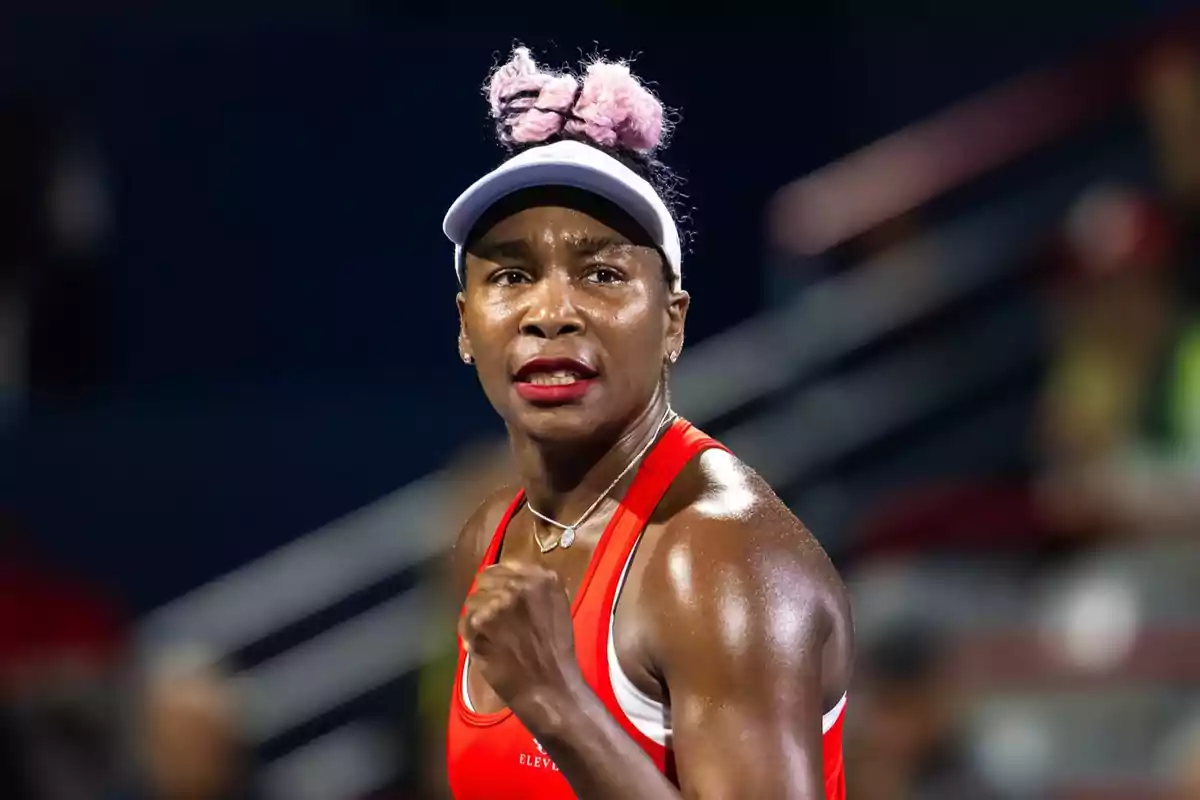 Venus Williams con ropa deportiva roja y visera blanca celebrando con el puño cerrado en una cancha de tenis. Venus Williams con ropa deportiva roja y visera blanca celebrando con el puño cerrado en una cancha de tenis.
