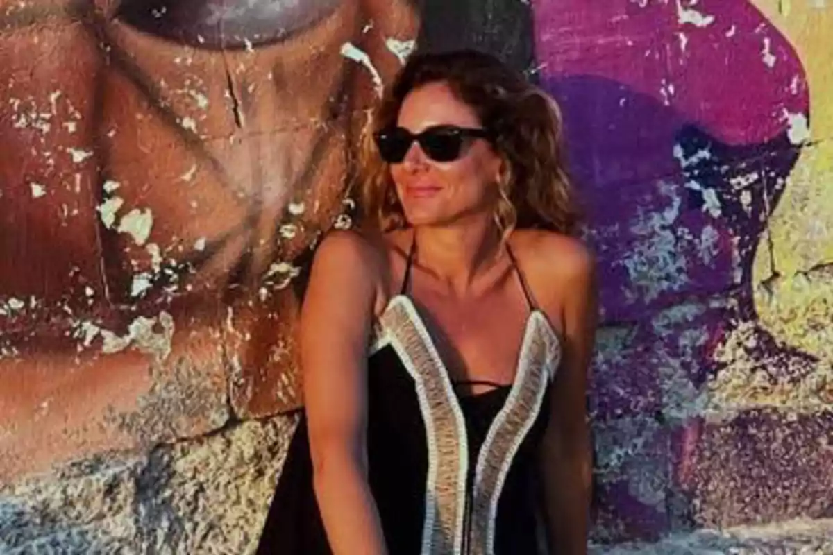 Verónica Dulanto con gafas de sol y vestido negro posando frente a una pared con grafiti colorido y desgastado Verónica Dulanto con gafas de sol y vestido negro posando frente a una pared con grafiti colorido y desgastado