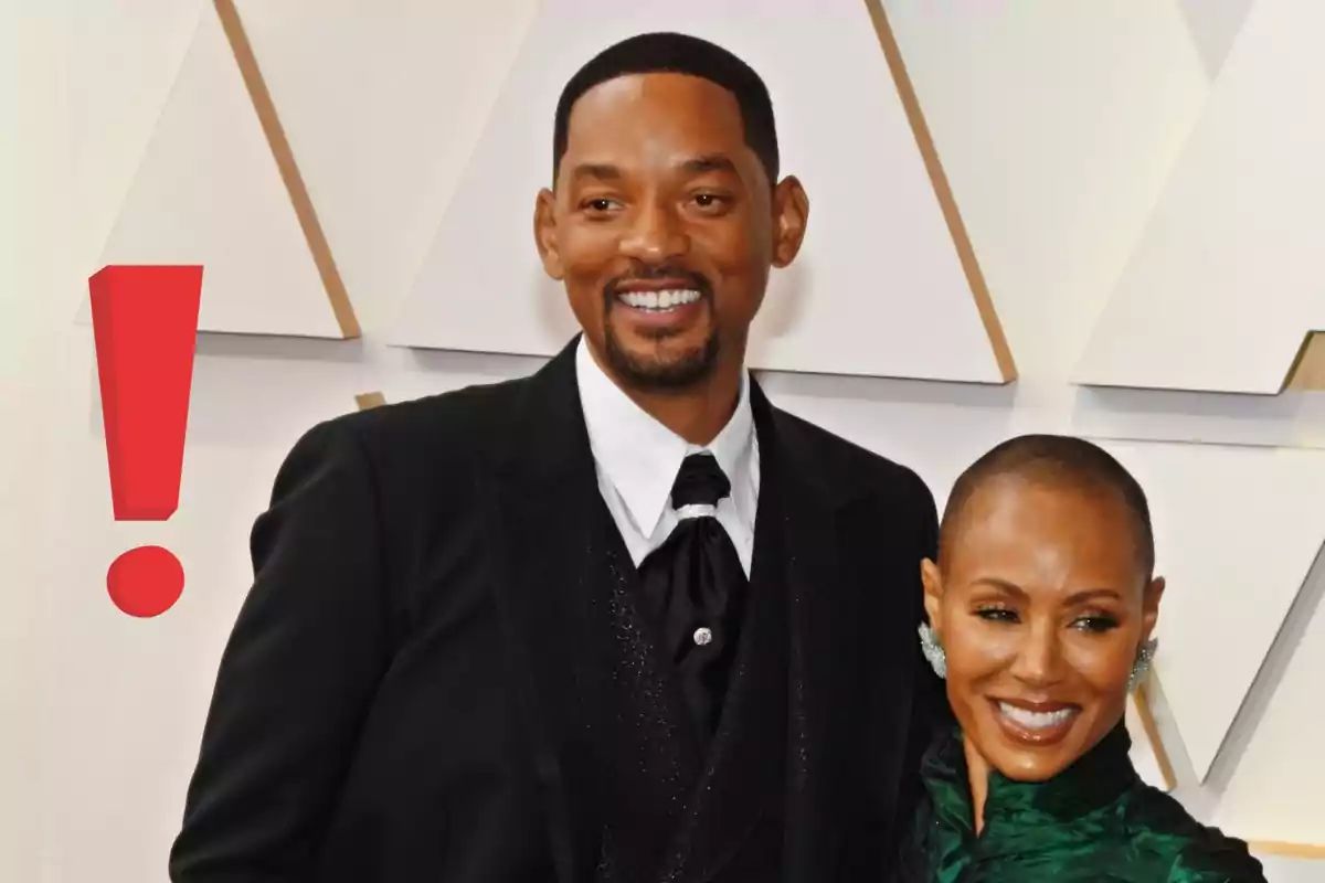 Will Smith y Jada Pinkett sonriente posando en una alfombra roja con un gran signo de exclamación rojo a la izquierda