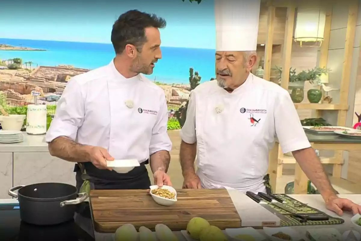 Dos xefs, que són Karlos Arguiñano i el seu fill, conversen en una cuina moderna mentre preparen ingredients sobre una taula de treball amb vistes al mar de fons. Dos xefs, que són Karlos Arguiñano i el seu fill, conversen en una cuina moderna mentre preparen ingredients sobre una taula de treball amb vistes al mar de fons.