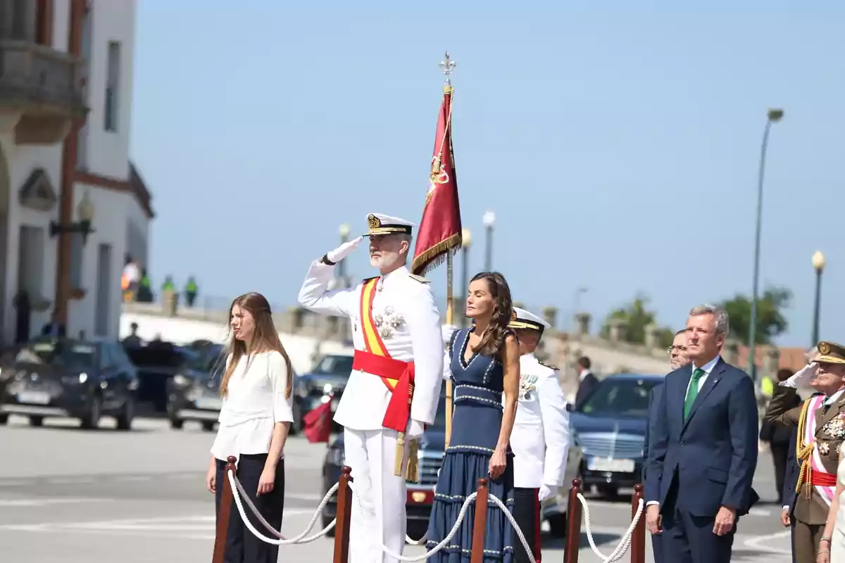 Several people dressed formally are participating in an outdoor ceremony; one of them is saluting militarily while holding a red flag. Several people dressed formally are participating in an outdoor ceremony; one of them is saluting militarily while holding a red flag.