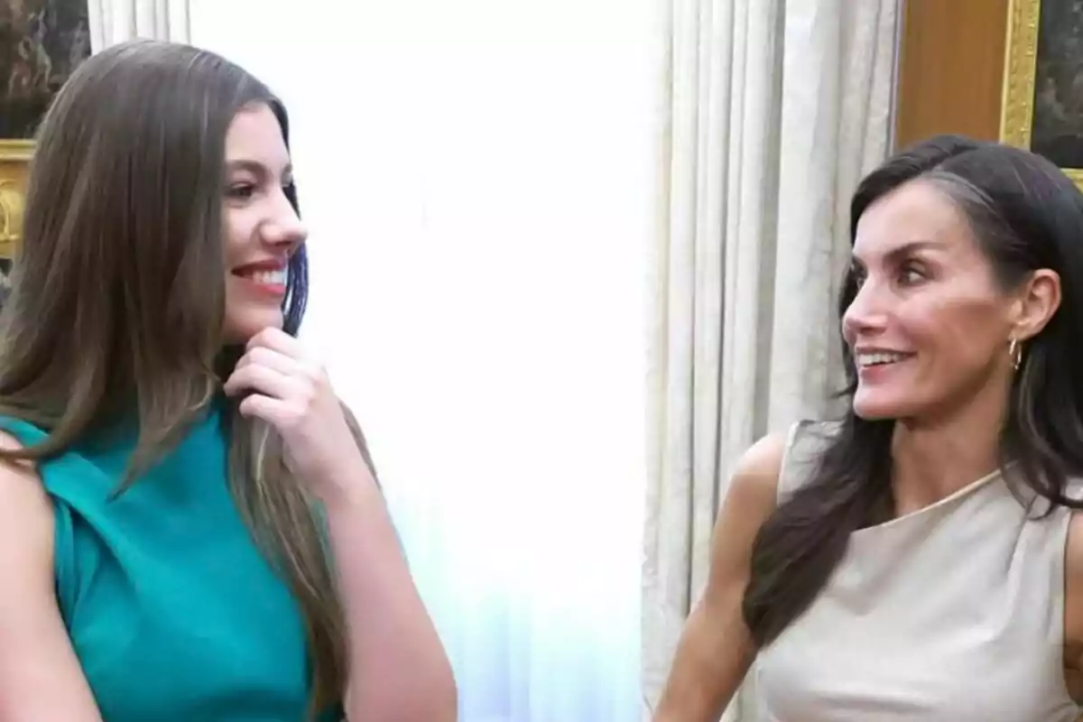 Dos mujeres, que son la reina Letizia y la infanta Sofía, sonríen y conversan mirándose la una a la otra en una habitación iluminada con cortinas claras de fondo. Dos mujeres, que son la reina Letizia y la infanta Sofía, sonríen y conversan mirándose la una a la otra en una habitación iluminada con cortinas claras de fondo.