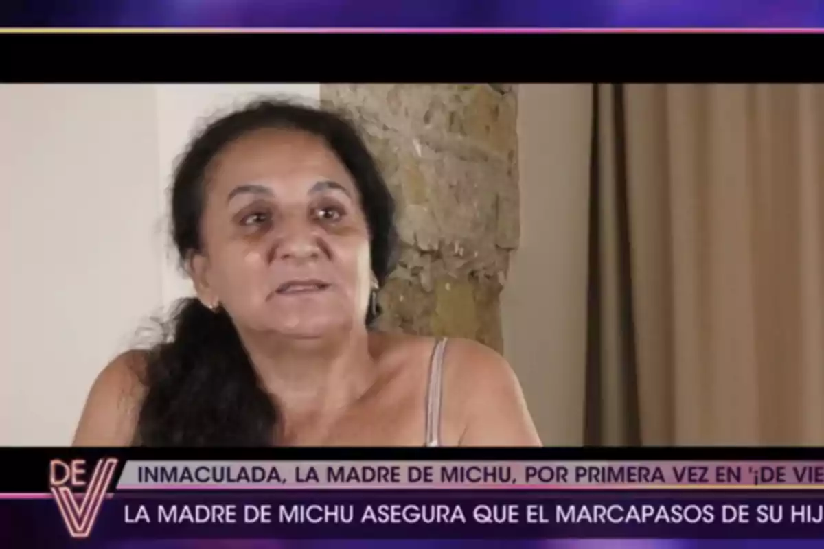 Inmaculada aparece en una entrevista televisiva con un fondo de pared de piedra y cortina, en la parte inferior de la imagen hay una franja con texto sobre la madre de Michu y un marcapasos. Inmaculada aparece en una entrevista televisiva con un fondo de pared de piedra y cortina, en la parte inferior de la imagen hay una franja con texto sobre la madre de Michu y un marcapasos.