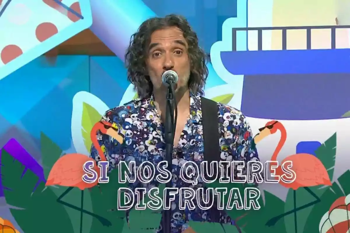 Joaquín Padilla vestido con una camisa colorida cantando frente a un micrófono con fondo colorido y la frase 'SI NOS QUIERES DISFRUTAR' rodeada de dibujos de flamencos y hojas. Joaquín Padilla vestido con una camisa colorida cantando frente a un micrófono con fondo colorido y la frase 'SI NOS QUIERES DISFRUTAR' rodeada de dibujos de flamencos y hojas.