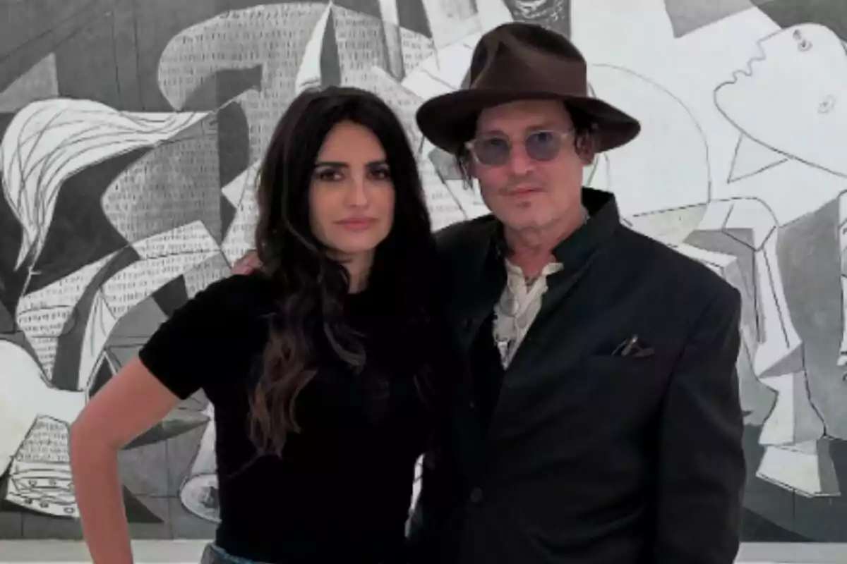 Two people pose together in front of a black and white painting: Johnny Depp and Penélope Cruz. Two people pose together in front of a black and white painting: Johnny Depp and Penélope Cruz.