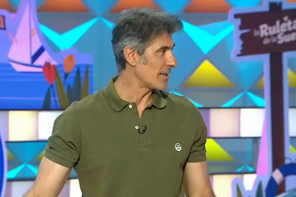 Jorge Fernández vestido con camiseta verde de manga corta en un set colorido de televisión. Jorge Fernández vestido con camiseta verde de manga corta en un set colorido de televisión.