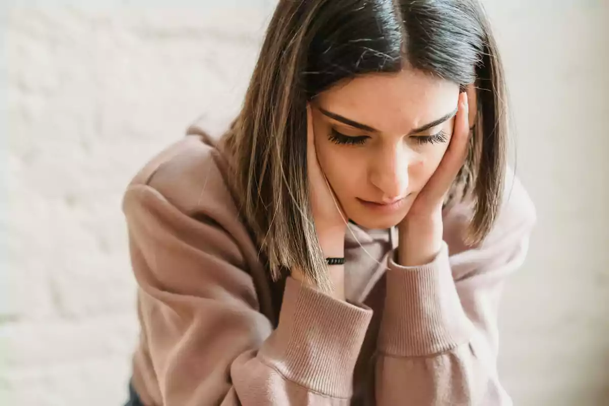 Young person with a worried expression resting their head in their hands Young person with a worried expression resting their head in their hands