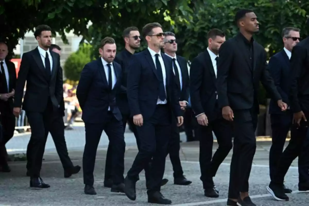 Group of men dressed in dark suits and ties walking together down the street under the shade of some trees, heading to Diogo Jota's funeral. Group of men dressed in dark suits and ties walking together down the street under the shade of some trees, heading to Diogo Jota's funeral.
