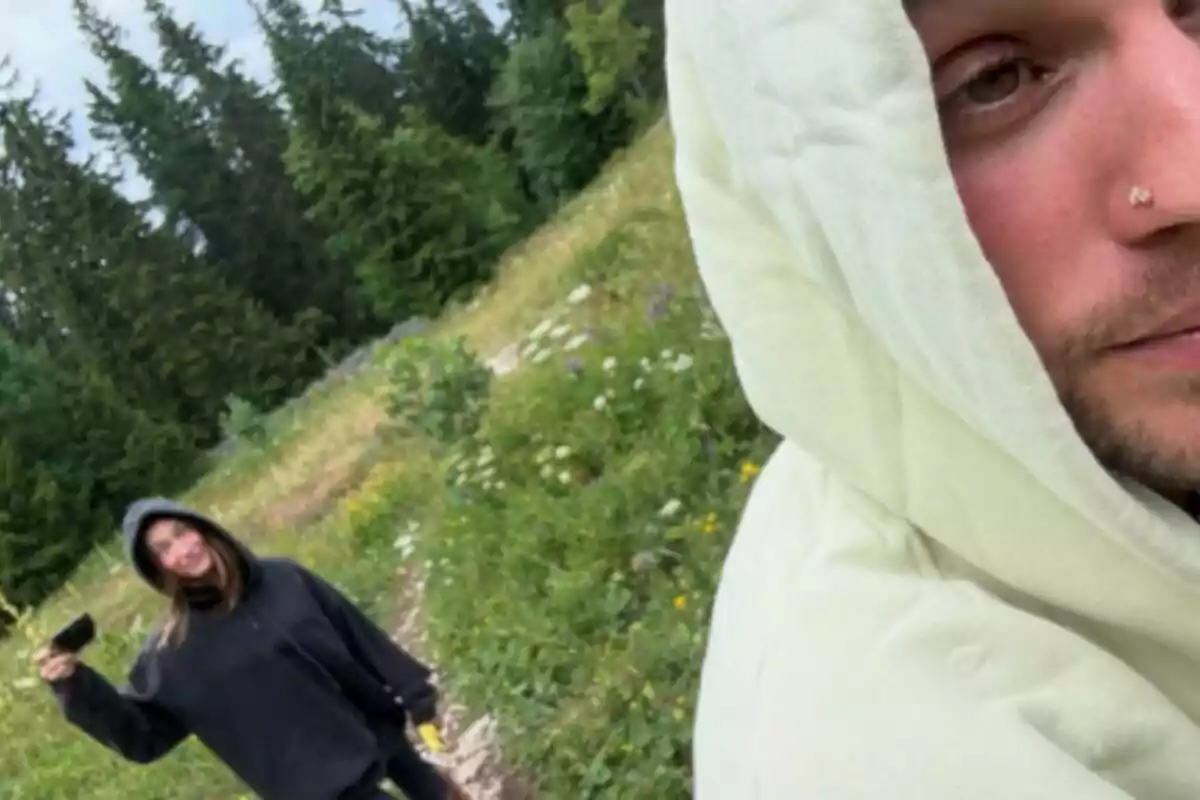Dos personas, que son Justin Bieber y Hailey Bieber, con sudaderas con capucha están al aire libre en un sendero rodeado de vegetación y árboles, una de ellas sostiene un objeto oscuro en la mano y la otra aparece en primer plano mirando a la cámara. Dos personas, que son Justin Bieber y Hailey Bieber, con sudaderas con capucha están al aire libre en un sendero rodeado de vegetación y árboles, una de ellas sostiene un objeto oscuro en la mano y la otra aparece en primer plano mirando a la cámara.