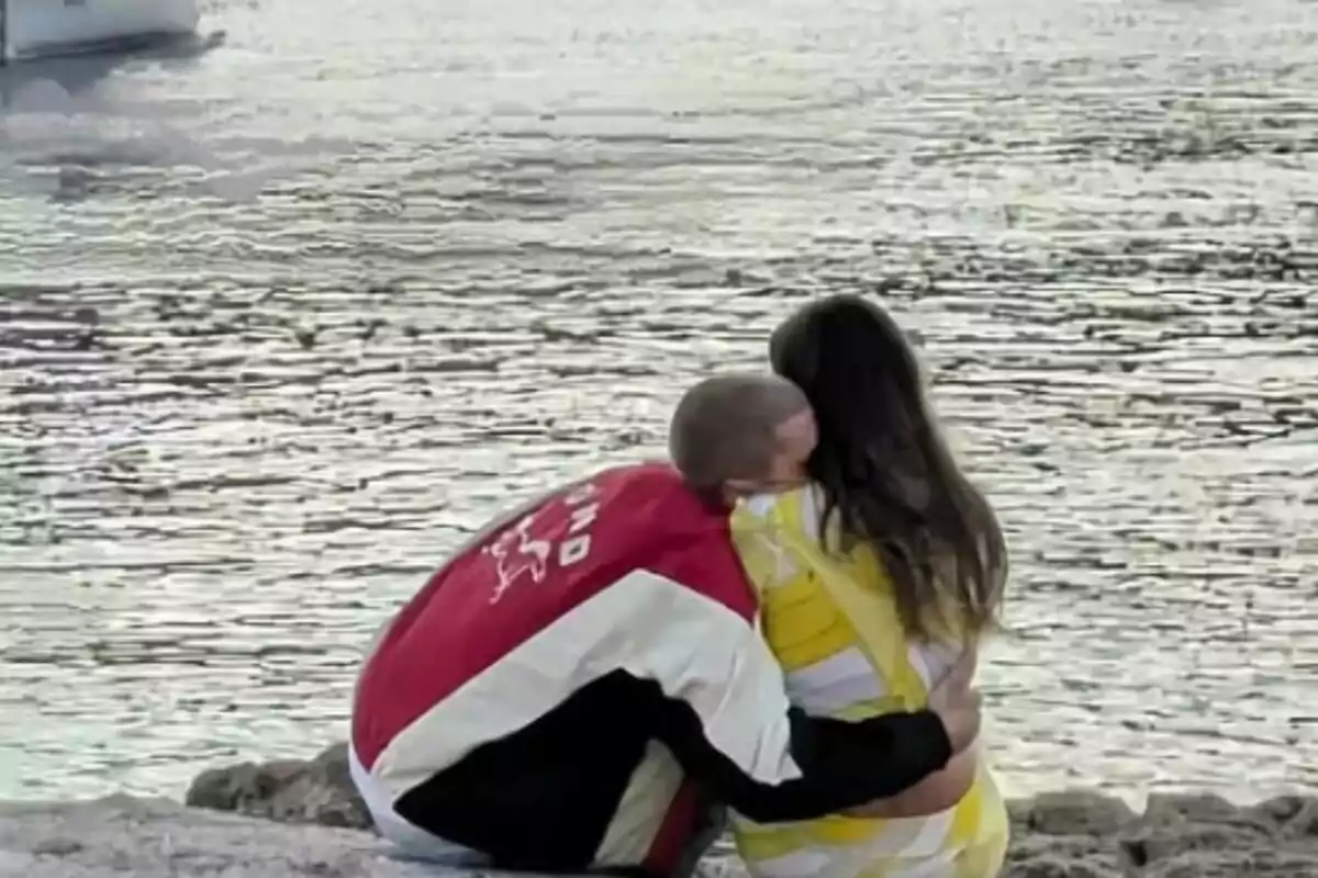 Pareja sentada junto al agua abrazándose mientras miran el paisaje, que son Justin y Hailey Bieber. Pareja sentada junto al agua abrazándose mientras miran el paisaje, que son Justin y Hailey Bieber.