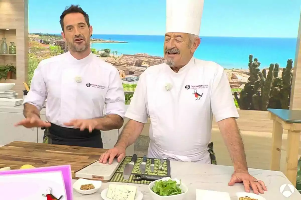 Dos xefs amb uniforme blanc, que són Karlos Arguiñano i el seu fill, són en una cuina de televisió amb vista al mar, sobre la taula hi ha ingredients i utensilis de cuina. Dos xefs amb uniforme blanc, que són Karlos Arguiñano i el seu fill, són en una cuina de televisió amb vista al mar, sobre la taula hi ha ingredients i utensilis de cuina.