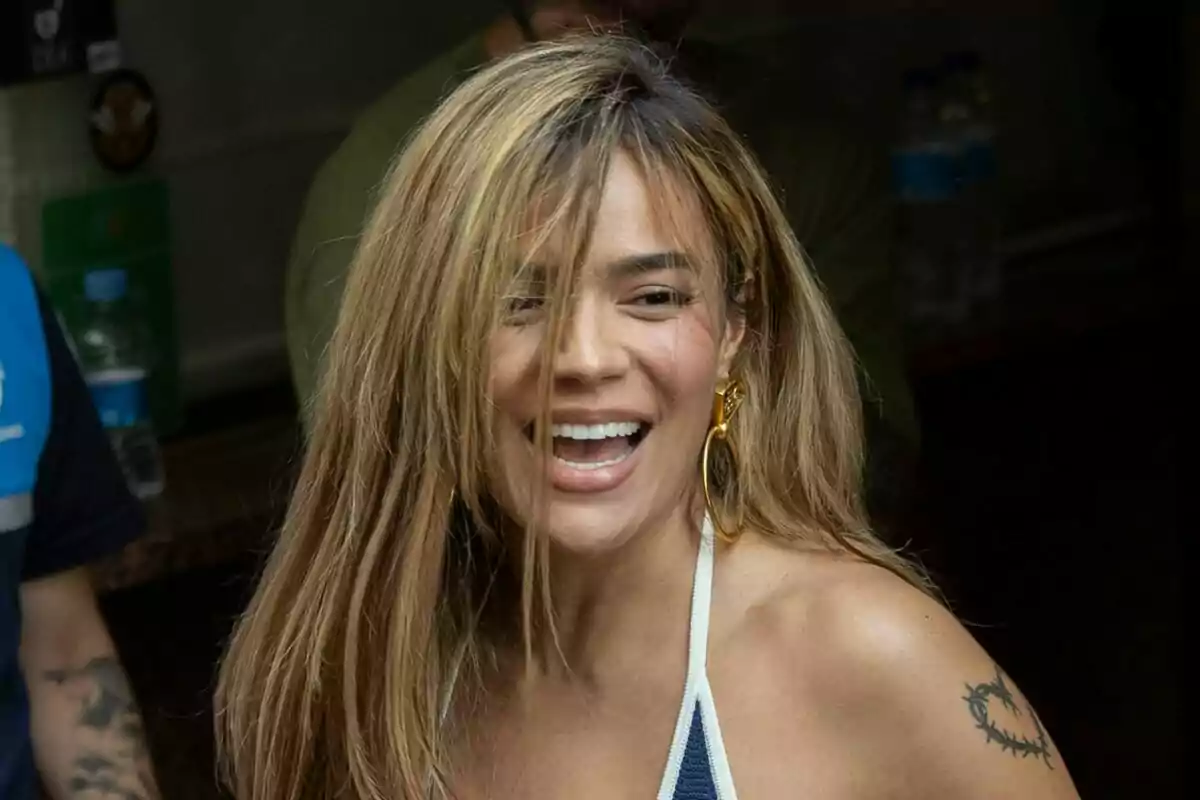 Karol G sonriendo con un pendiente dorado grande y un tatuaje en el brazo izquierdo. Karol G sonriendo con un pendiente dorado grande y un tatuaje en el brazo izquierdo.