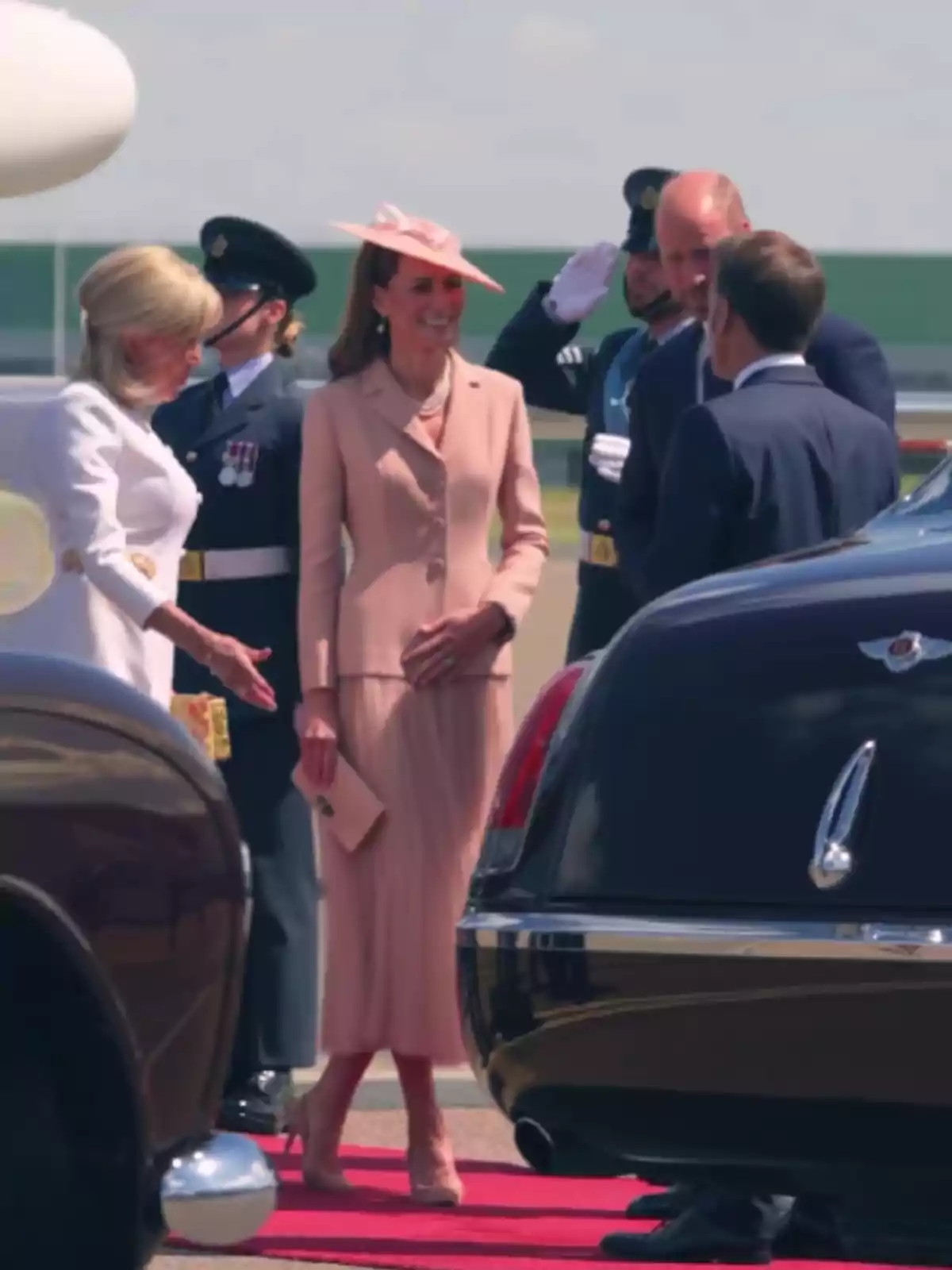 Diverses persones elegantment vestides es saluden al costat de cotxes de luxe sobre una catifa vermella en un esdeveniment formal a l’aire lliure. Diverses persones elegantment vestides es saluden al costat de cotxes de luxe sobre una catifa vermella en un esdeveniment formal a l’aire lliure.