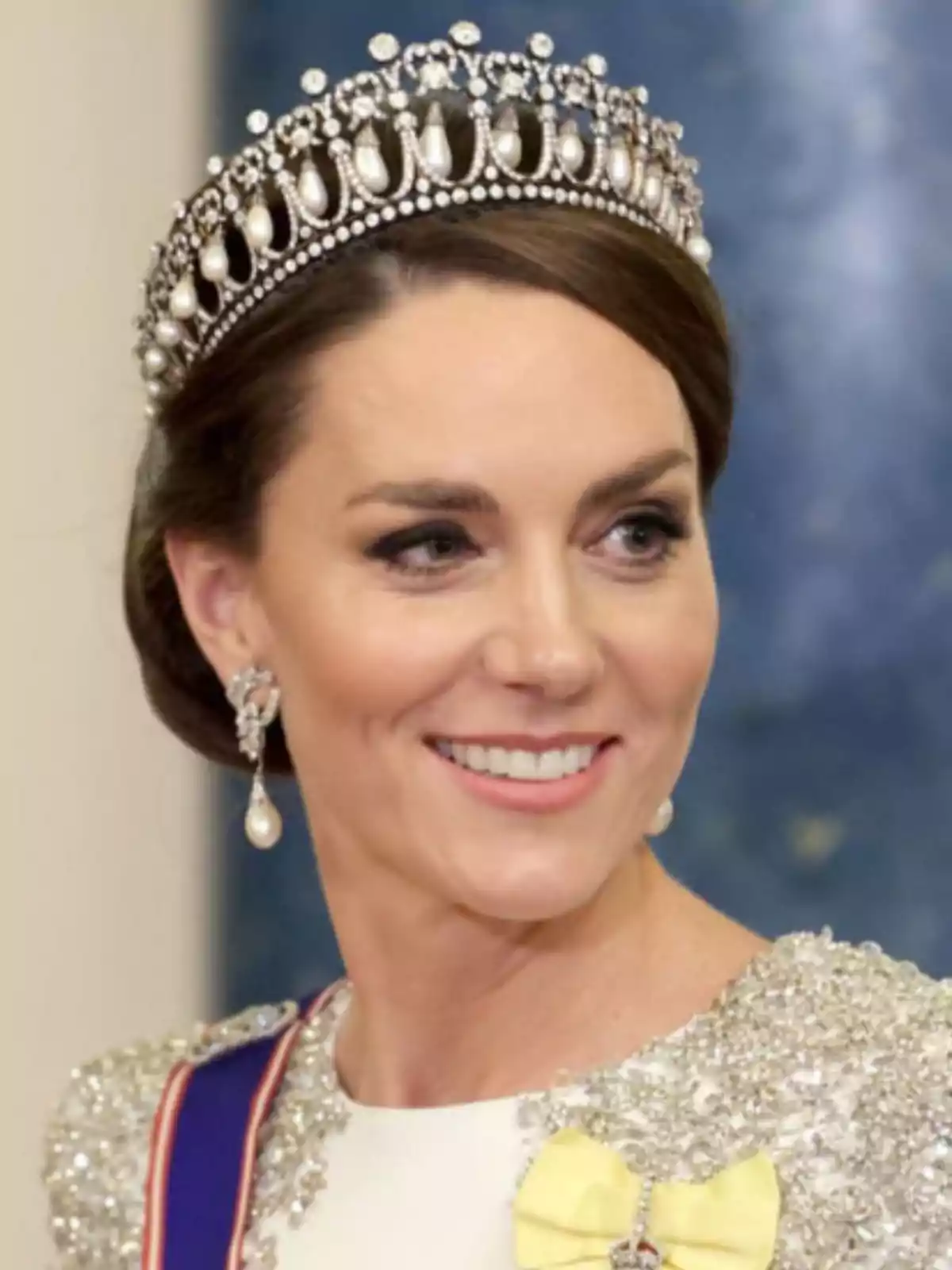 Dona somrient amb tiara de perles i diamants, vestit elegant amb detalls brillants i monyo groc Dona somrient amb tiara de perles i diamants, vestit elegant amb detalls brillants i monyo groc