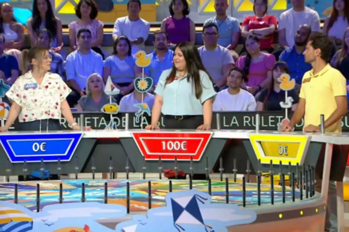 Tres concursants participen en un programa de jocs de televisió amb un públic de fons i un panell de premis on la concursant del centre porta l'avantatge amb 100 euros. Captura de 'La Ruleta de la Suerte' Tres concursants participen en un programa de jocs de televisió amb un públic de fons i un panell de premis on la concursant del centre porta l'avantatge amb 100 euros. Captura de 'La Ruleta de la Suerte'