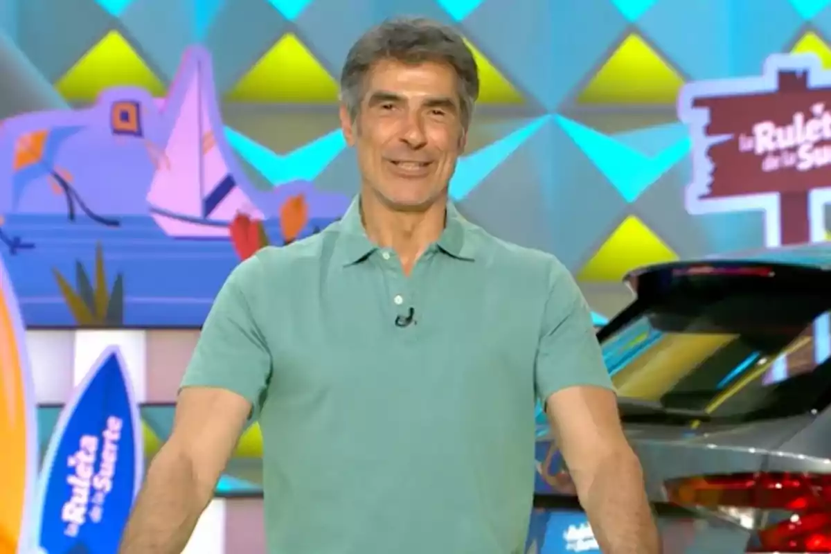 Jorge Fernández amb samarreta verd clar somriu en un plató de televisió colorit amb decoracions i un cotxe al fons. Captura de 'La Ruleta de la Suerte' Jorge Fernández amb samarreta verd clar somriu en un plató de televisió colorit amb decoracions i un cotxe al fons. Captura de 'La Ruleta de la Suerte'