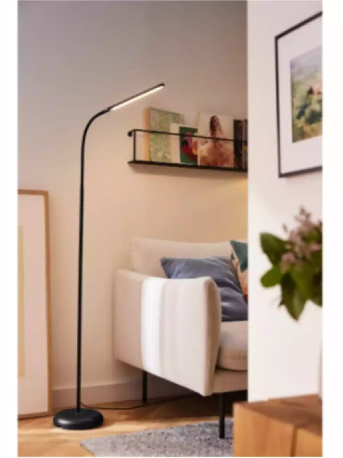 Làmpada de peu negra al costat d’un sofà beix amb coixins en una sala decorada amb quadres i prestatgeria de llibres Làmpada de peu negra al costat d’un sofà beix amb coixins en una sala decorada amb quadres i prestatgeria de llibres