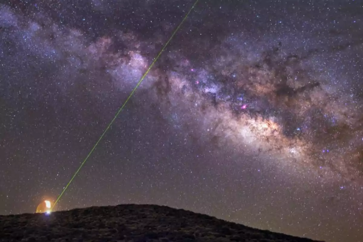 A green laser beam points toward the starry sky with the Milky Way visible above a dark hill. A green laser beam points toward the starry sky with the Milky Way visible above a dark hill.