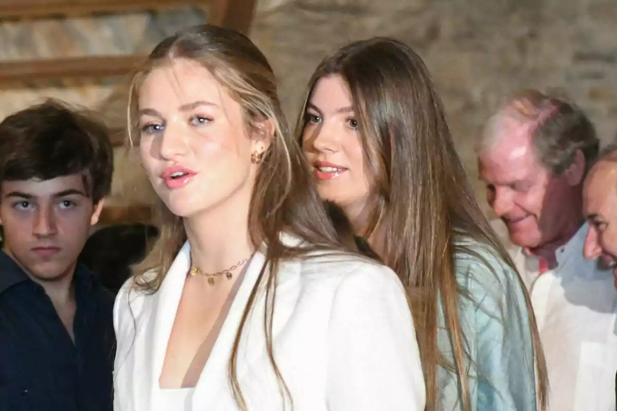 Grup de persones joves i adultes en un esdeveniment social amb fons de paret de pedra, dues de les quals la princesa Leonor i la infanta Sofia.