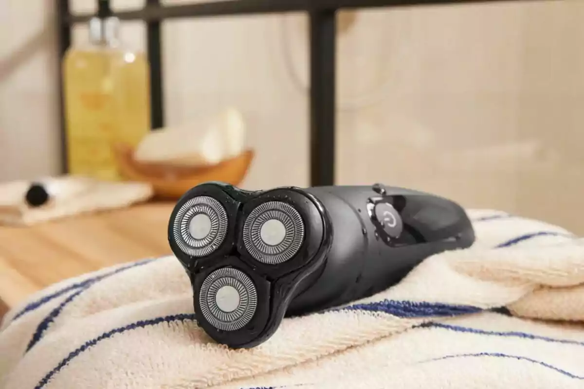 Afeitadora elèctrica negra amb capçals circulars sobre una tovallola blanca amb ratlles blaves en un bany Afeitadora elèctrica negra amb capçals circulars sobre una tovallola blanca amb ratlles blaves en un bany