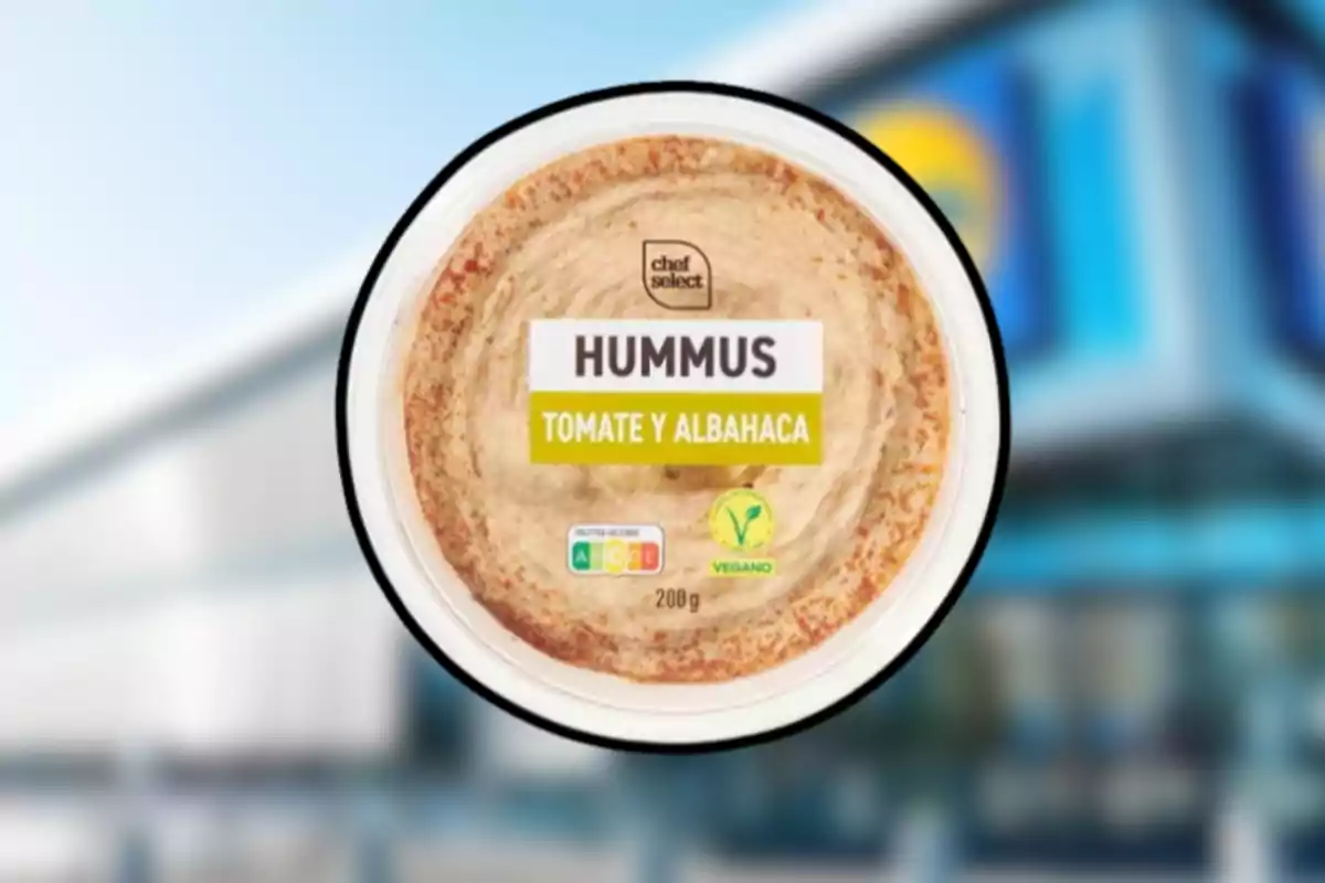 Envàs d’hummus sabor tomàquet i alfàbrega de la marca Chef Select amb etiqueta vegana sobre un fons desenfocat de supermercat. Envàs d’hummus sabor tomàquet i alfàbrega de la marca Chef Select amb etiqueta vegana sobre un fons desenfocat de supermercat.