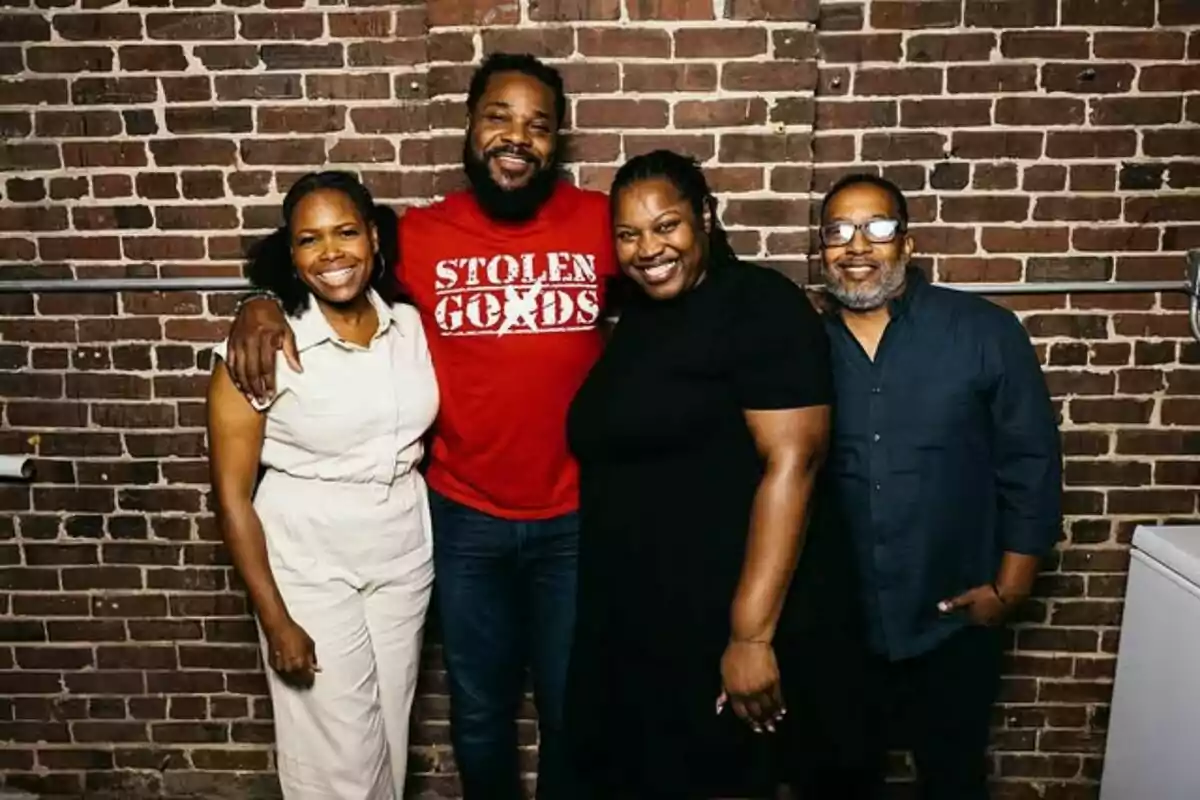 Four people smile and pose together in front of a brick wall. Four people smile and pose together in front of a brick wall.