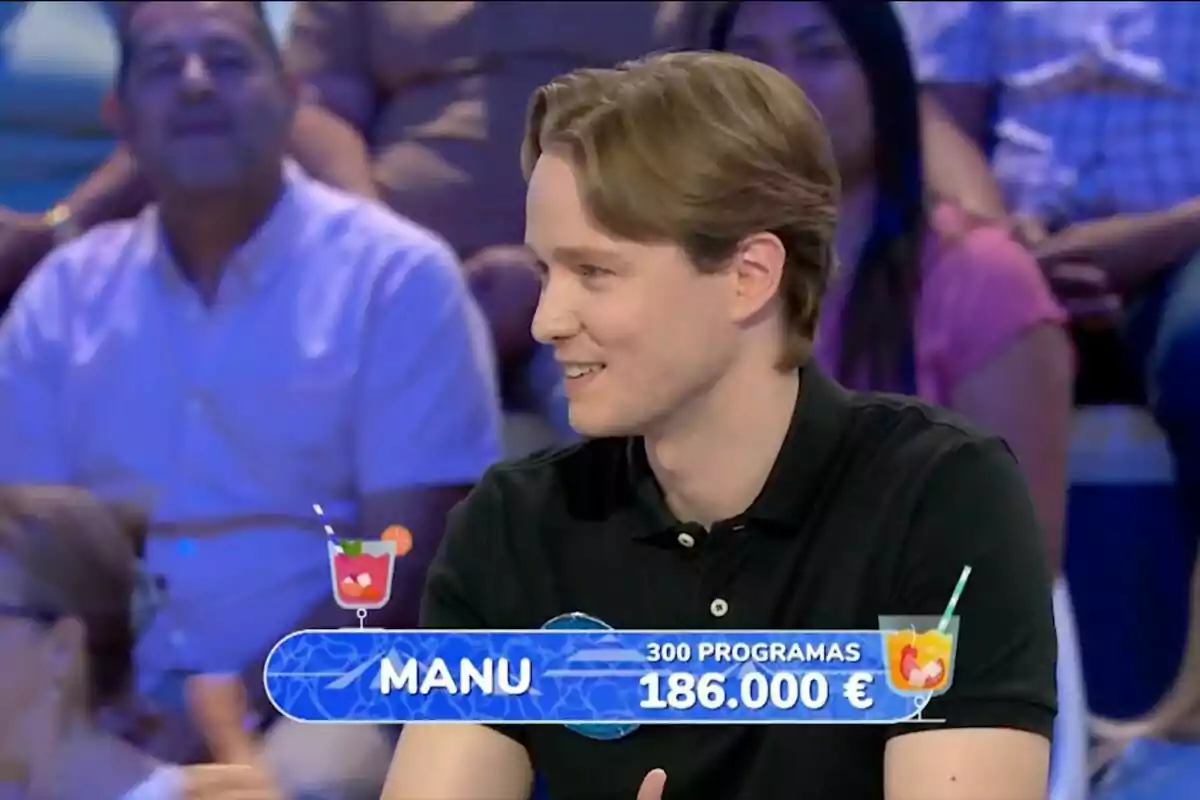 Un jove amb camisa negra somriu mentre participa en un concurs televisiu, amb un rètol que mostra el seu nom, la quantitat de programes i els diners acumulats, envoltat de públic al fons. Un jove amb camisa negra somriu mentre participa en un concurs televisiu, amb un rètol que mostra el seu nom, la quantitat de programes i els diners acumulats, envoltat de públic al fons.