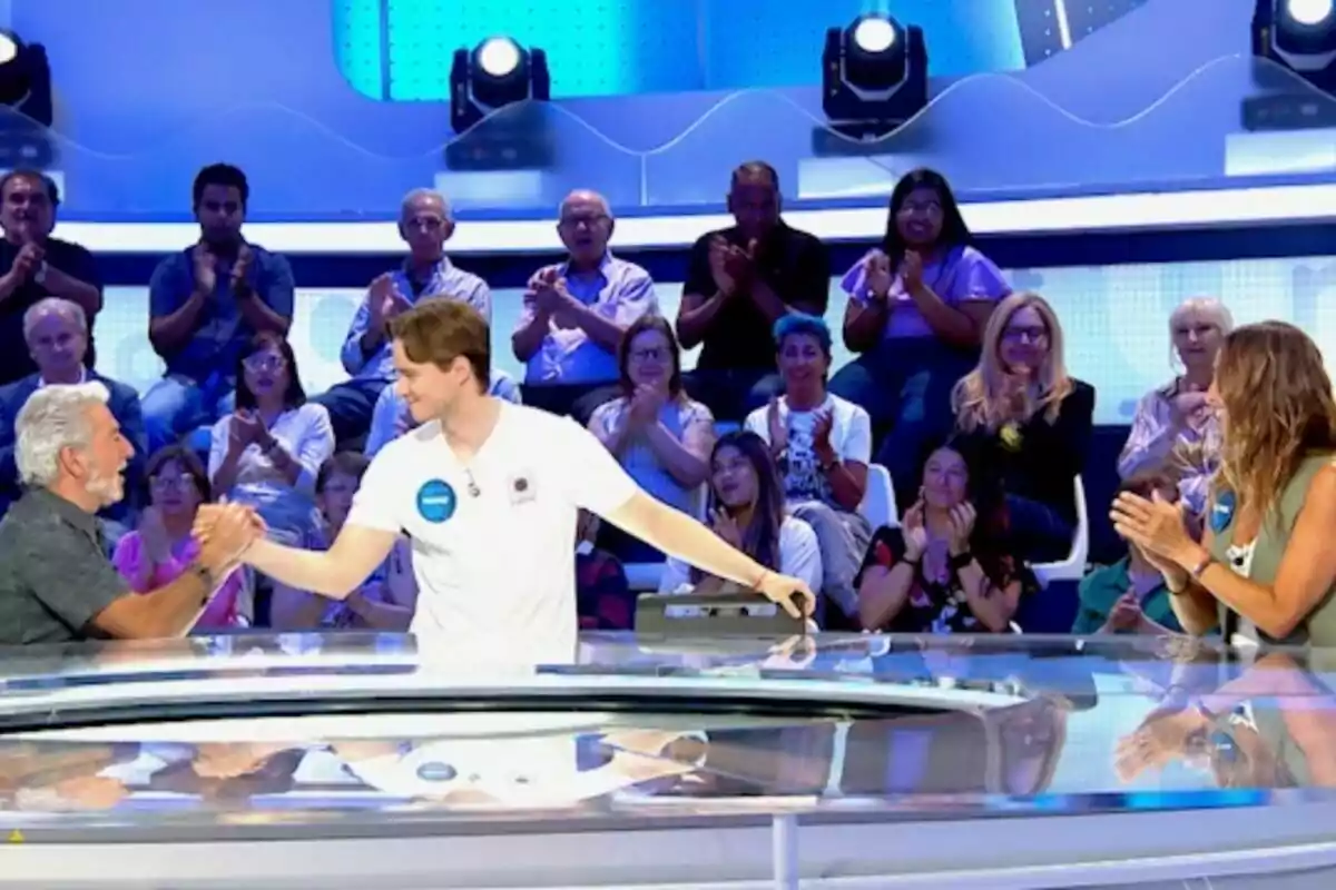 Dos concursants es donen la mà al centre d’un plató de televisió mentre el públic de ‘Pasapalabra’ aplaudeix des de les grades. Dos concursants es donen la mà al centre d’un plató de televisió mentre el públic de ‘Pasapalabra’ aplaudeix des de les grades.