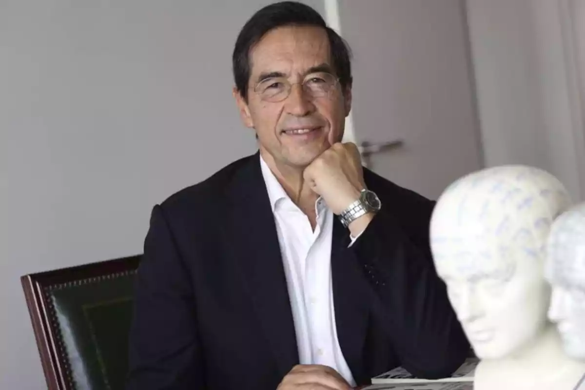 Mario Alonso Puig assegut en una oficina, recolzant la barbeta a la mà, amb bustos de models anatòmics en primer pla.