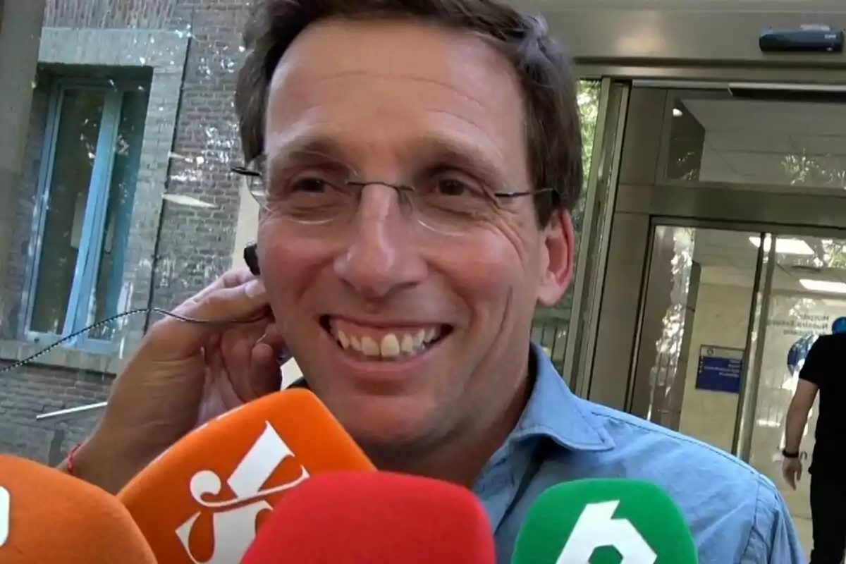 José Luís Martínez Almeida, smiling and wearing glasses, being interviewed by several media outlets in front of a hospital. José Luís Martínez Almeida, smiling and wearing glasses, being interviewed by several media outlets in front of a hospital.