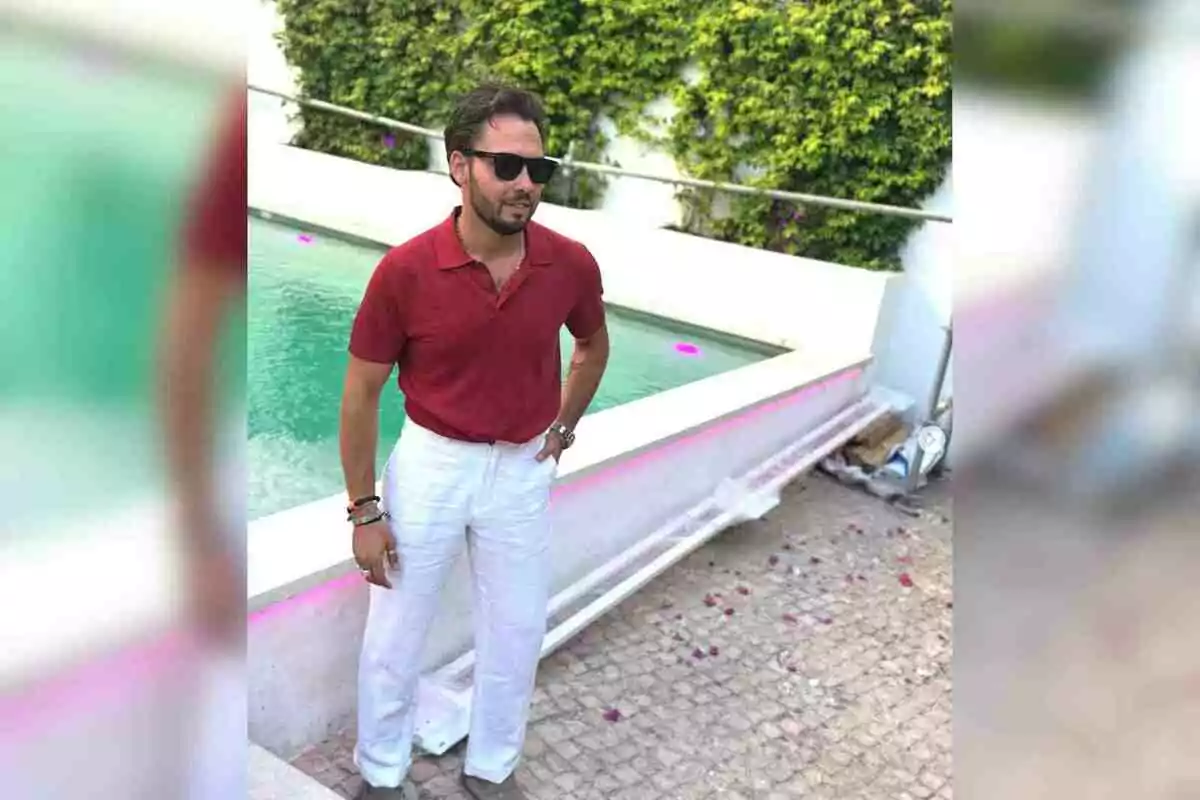 José Antonio Avilés con gafas de sol, camisa roja y pantalón blanco de pie junto a una piscina en un entorno al aire libre con vegetación al fondo José Antonio Avilés con gafas de sol, camisa roja y pantalón blanco de pie junto a una piscina en un entorno al aire libre con vegetación al fondo