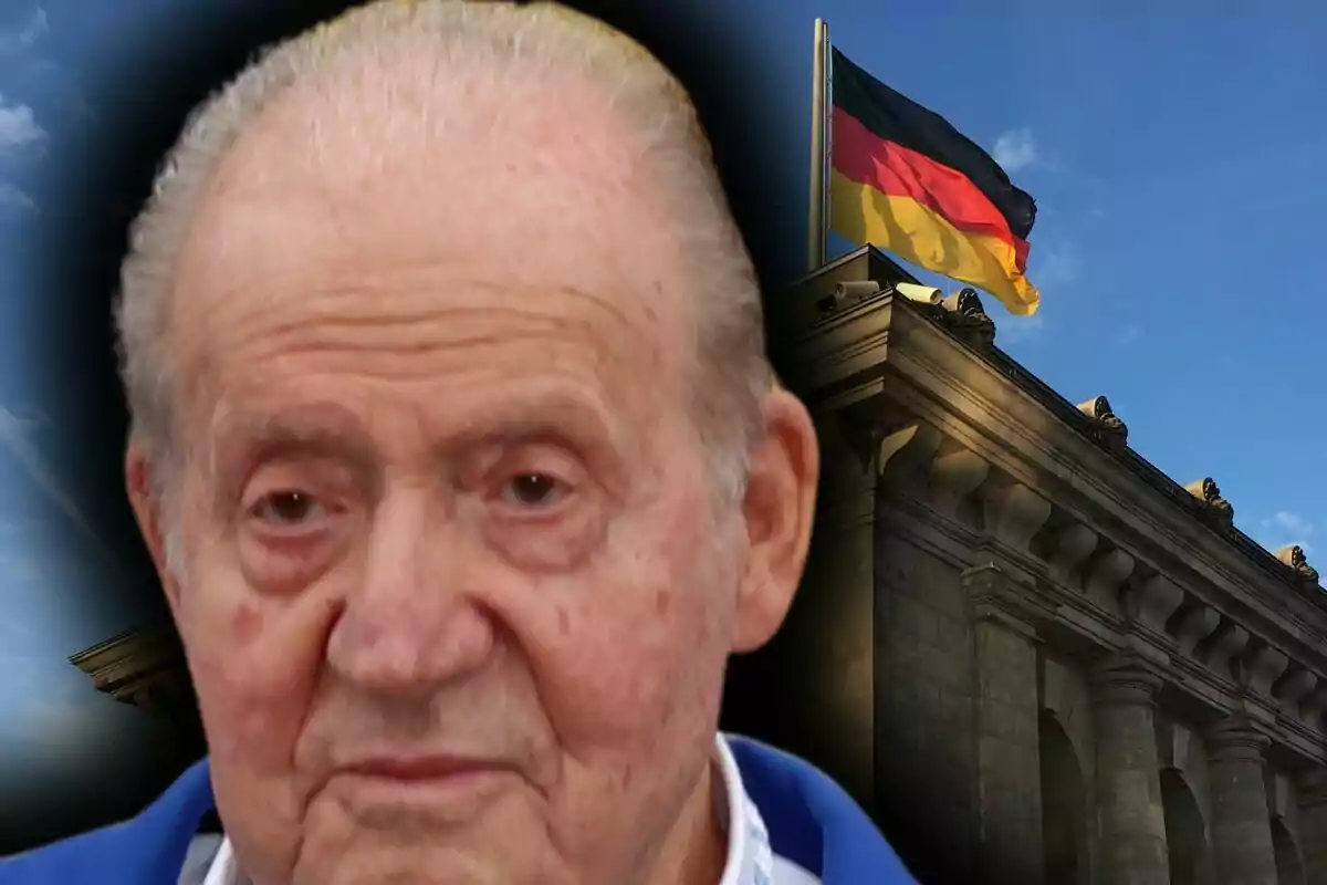 Close-up of Juan Carlos I with a serious expression and, in the background, a building with a German flag waving.