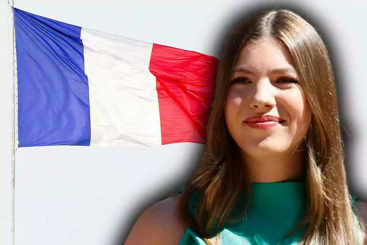 La infanta Sofía de cabello largo y lacio sonríe frente a una bandera de Francia ondeando sobre un fondo claro
