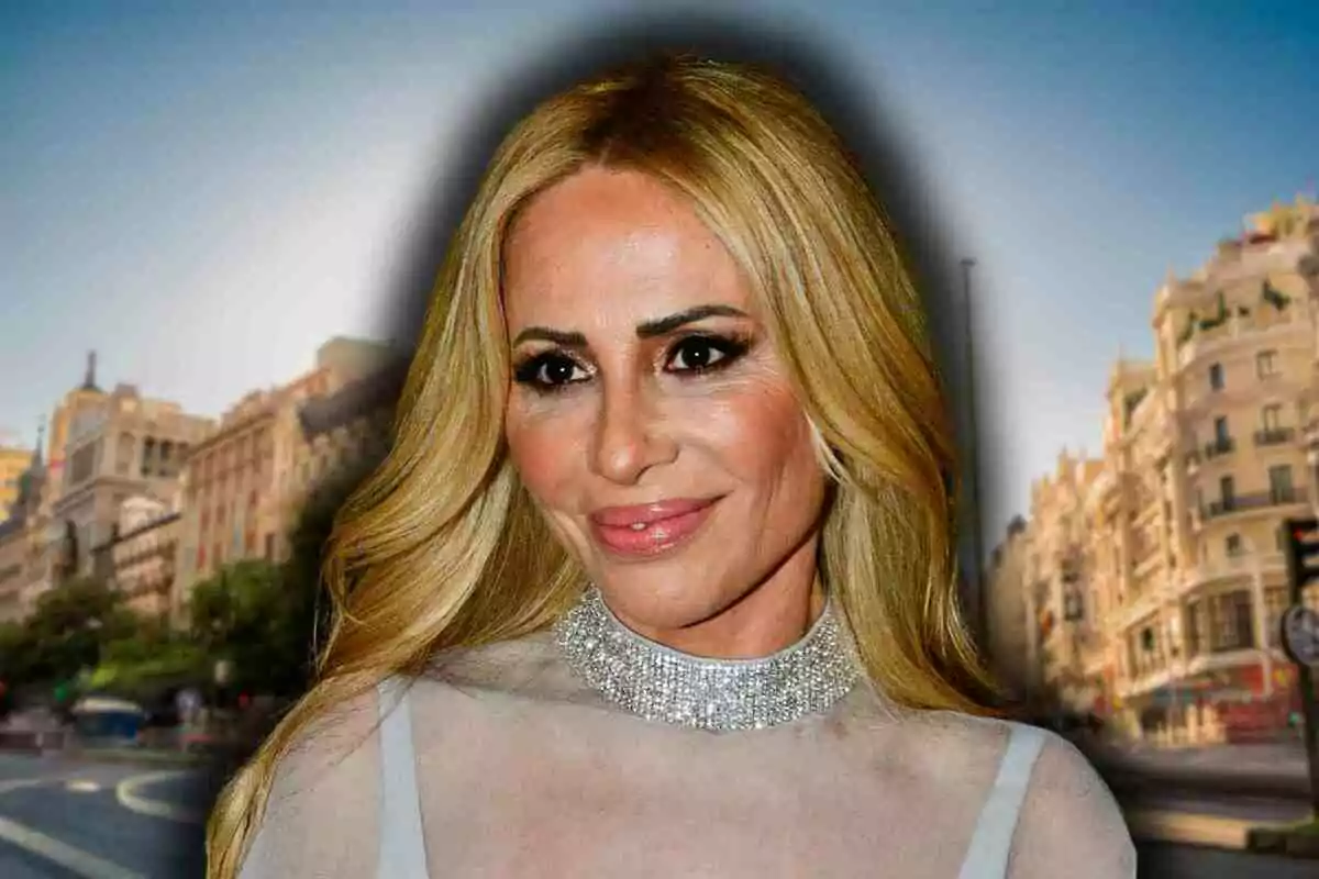 Marta Sánchez con vestido claro y collar brillante posando frente a un fondo urbano desenfocado