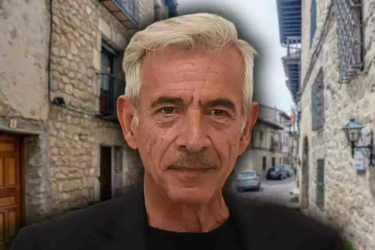 Inmanol Arias de cabello canoso y bigote con expresión seria posando frente a una calle de un pueblo de piedra