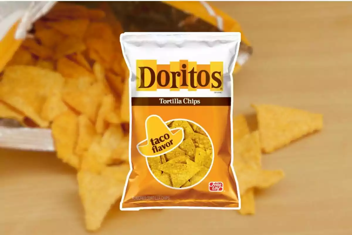 Bolsa de Doritos sabor taco sobre una mesa con totopos esparcidos alrededor Bolsa de Doritos sabor taco sobre una mesa con totopos esparcidos alrededor