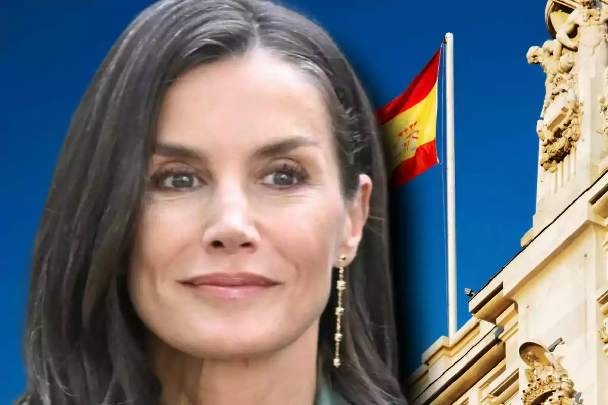Queen Letizia with a serious expression in front of a historic building and a Spanish flag waving in the background.