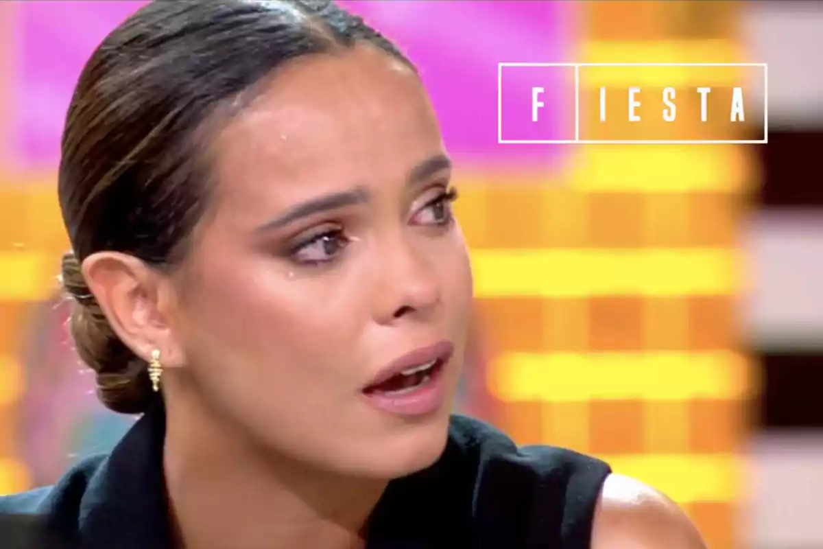 Gloria Camila con expresión de tristeza y lágrimas en el rostro durante un programa de televisión llamado Fiesta con fondo colorido desenfocado