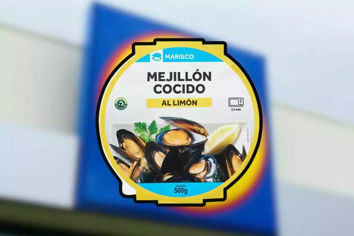 Envàs de musclo cuit al llimona de 500 grams amb imatge de musclos, una rodanxa de llimona i julivert, sobre un fons desenfocat blau i blanc. Envàs de musclo cuit al llimona de 500 grams amb imatge de musclos, una rodanxa de llimona i julivert, sobre un fons desenfocat blau i blanc.