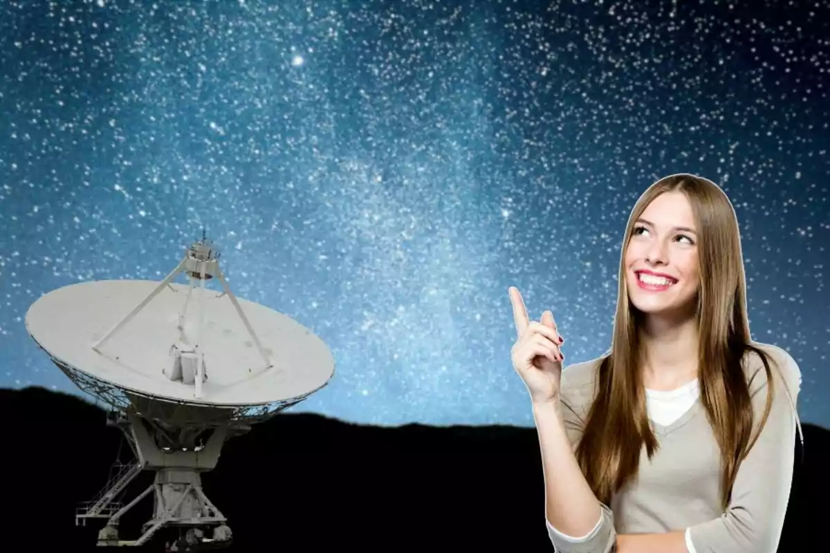 Dona somrient assenyalant cap al cel estrellat al costat d’una antena parabòlica