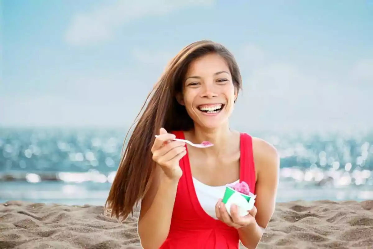 Dona somrient menjant gelat a la platja amb el mar de fons